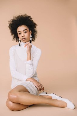 şık beyaz elbise ve ayakkabı bej katta oturan genç Afro-Amerikan kadın