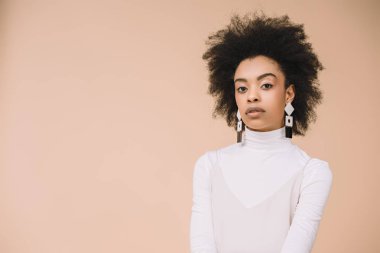 attractive young woman in white turtleneck looking at camera isolated on beige clipart