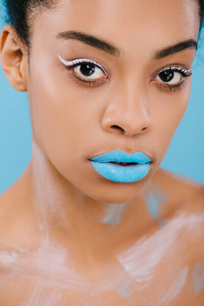 close-up portrait of young african american woman with creative makeup and perfect skin looking at camera isolated on blue