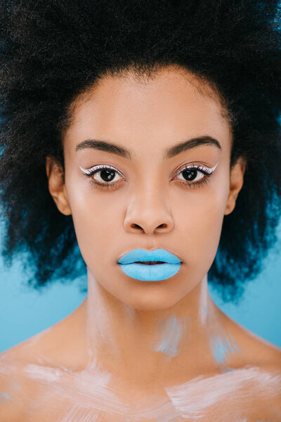 young woman with creative makeup and blue lips looking at camera isolated on blue