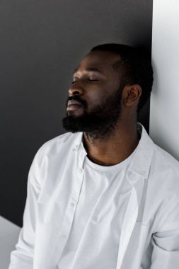 yakışıklı şık Afrikalı-Amerikalı adam kapalı gözler ile duvara yaslanmış Beyaz giysili