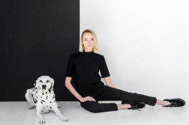 attractive stylish blonde woman in black clothes sitting near black and white wall with dalmatian dog clipart