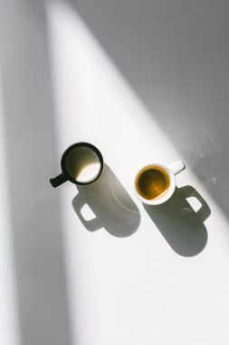 top view of black and white cups of milk and coffee on white surface clipart