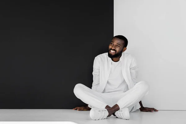 Sorrindo Elegante Homem Americano Africano Sentado Chão Perto Parede Preta — Fotografia de Stock