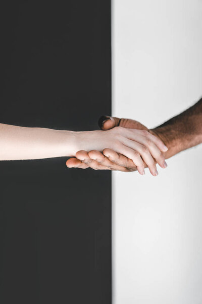 cropped image of multicultural couple holding hands near black and white wall
