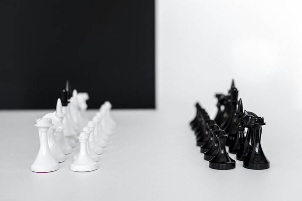 chess figures in rows on white tabletop near black and white wall