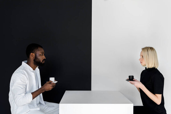 side view of multicultural couple sitting with cups of coffee