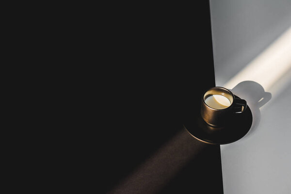 высокий угол обзора чашки молока в черной чашке на черно-белой поверхности с солнечным светом
