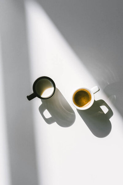 top view of black and white cups of milk and coffee on white surface