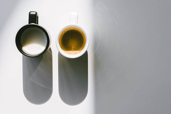 top view of black and white cups of milk and coffee on white tabletop