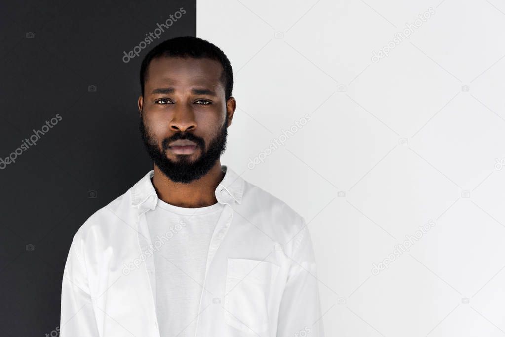 portrait of handsome stylish african american man in white clothes near black and white wall