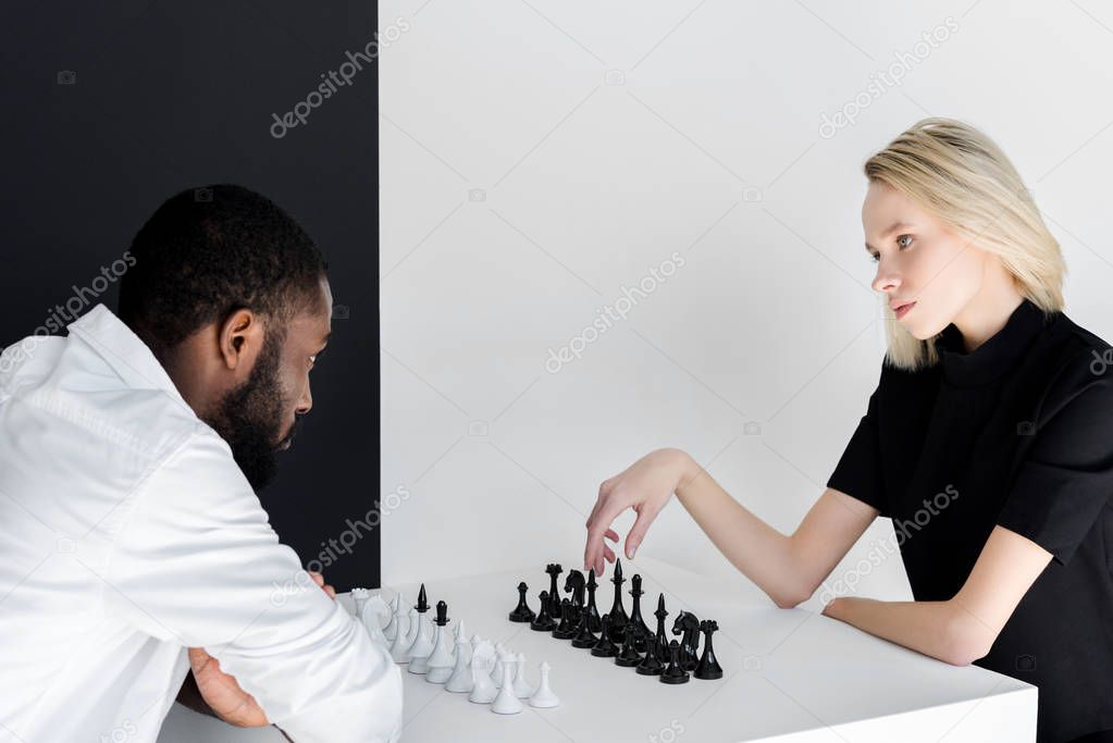 multicultural couple playing chess near black and white wall