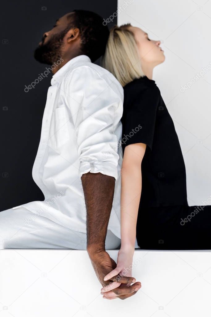 african american boyfriend and blonde girlfriend holding hands on white cube