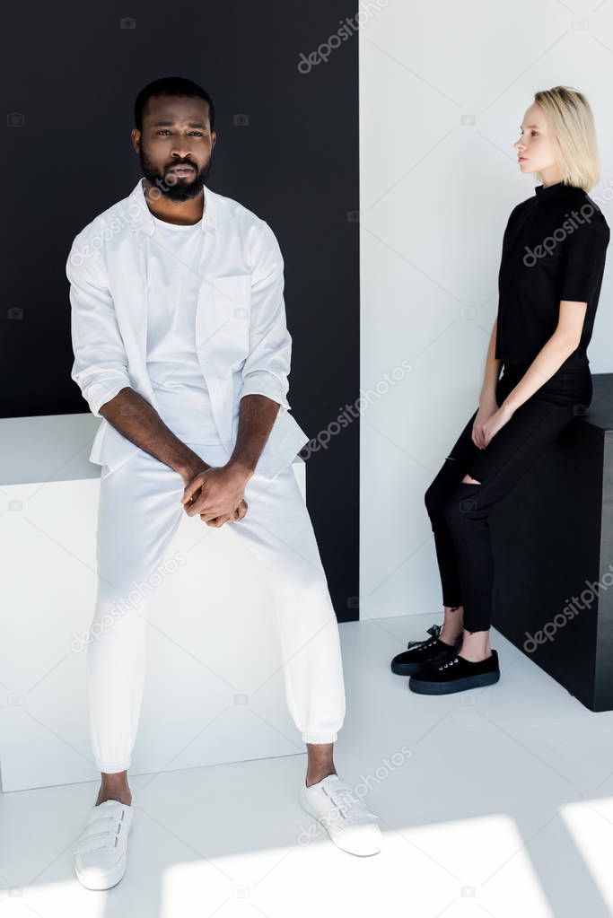 multicultural couple sitting on black and white cubes