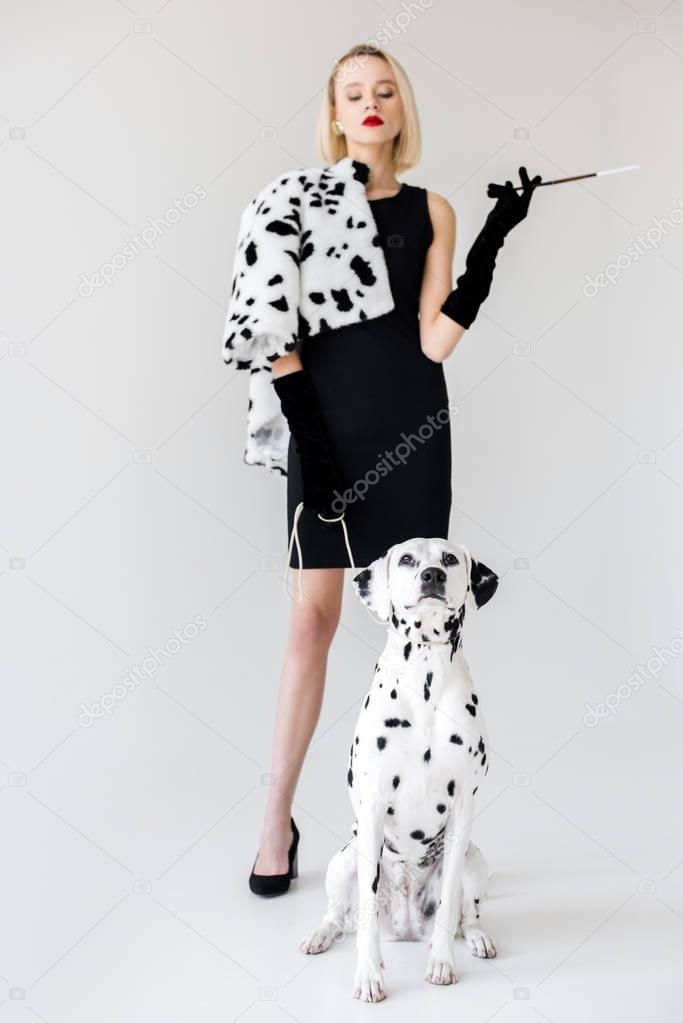 attractive stylish blonde woman in black dress looking at dalmatian dog on white