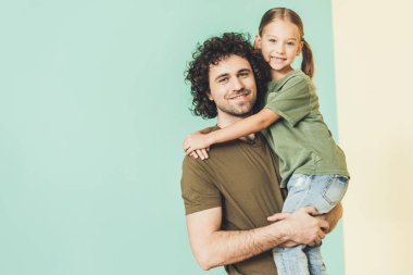 Sevimli küçük kızını taşıyan ve kameraya gülümseyen mutlu baba