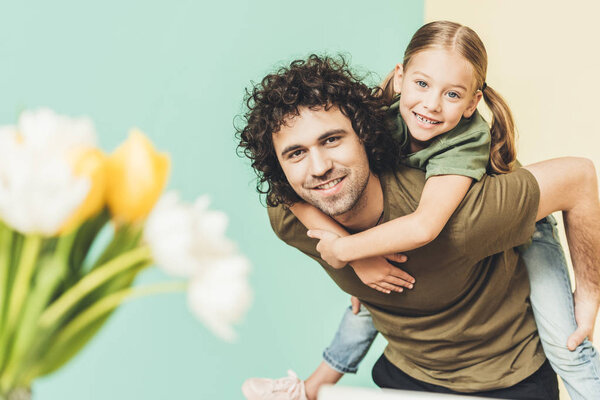 selective focus of father piggybacking adorable happy daughter and smiling at camera