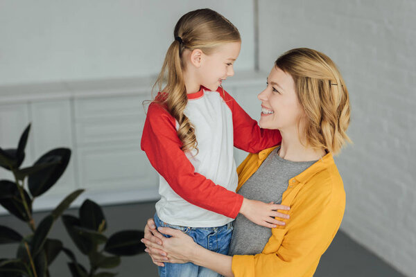 красивая счастливая мать и дочь обнимают и улыбаются друг другу дома
