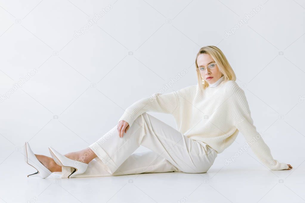 attractive stylish blonde woman in white clothes sitting on white floor