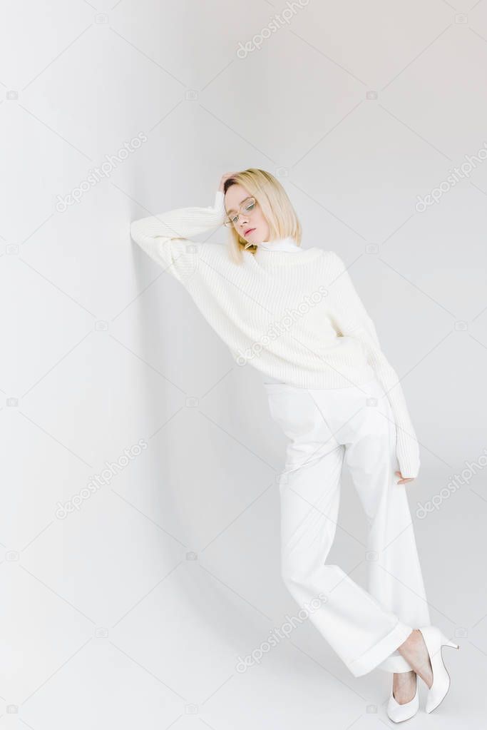 beautiful stylish blonde girl in white clothes leaning on white wall