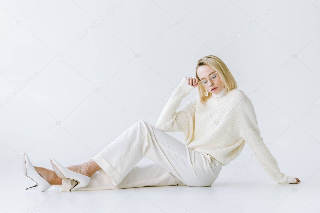 beautiful stylish blonde woman in white clothes sitting on white floor