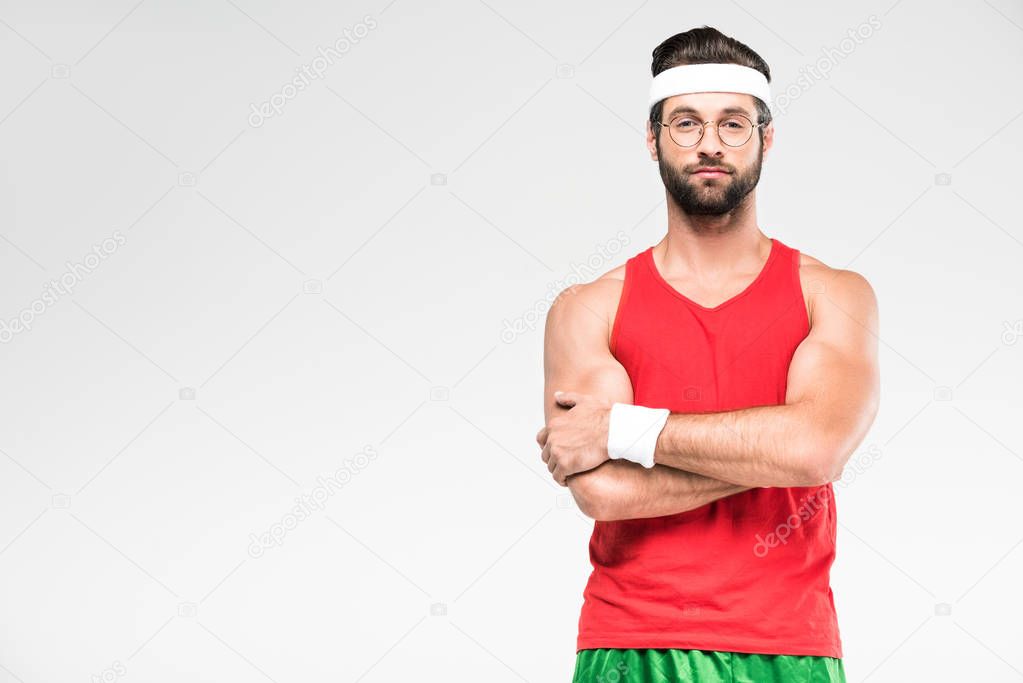 handsome sportsman posing in retro sportswear and sunglasses with crossed arms, isolated on white