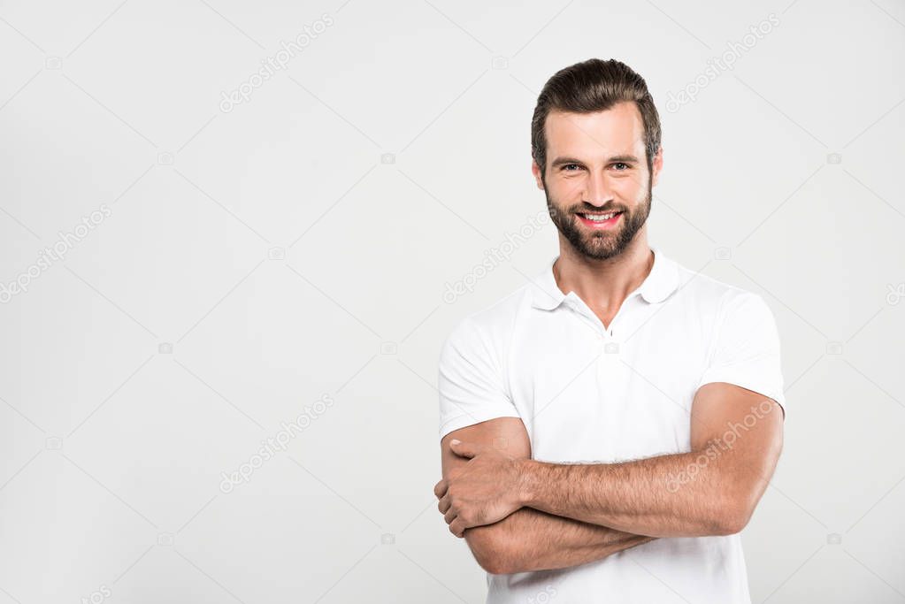 handsome smiling man posing in white with crossed arms, isolated on grey