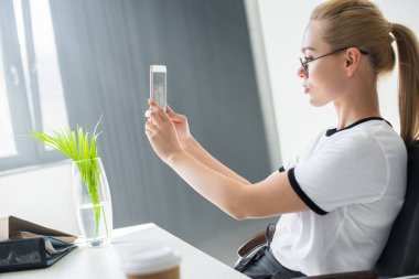 güzel genç sarışın işkadını selfie ile smartphone içinde göreve yan görünüm 