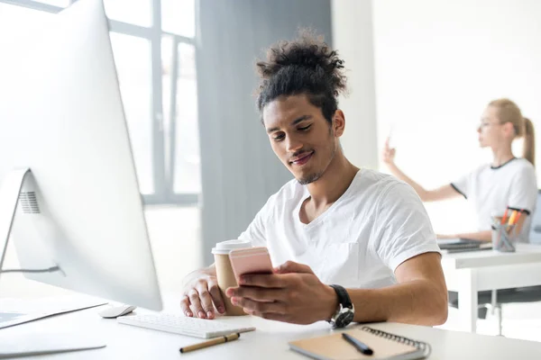 Leende Ung Afroamerikanska Man Använder Smartphone Medan Sitter Arbetsplatsen — Stockfoto