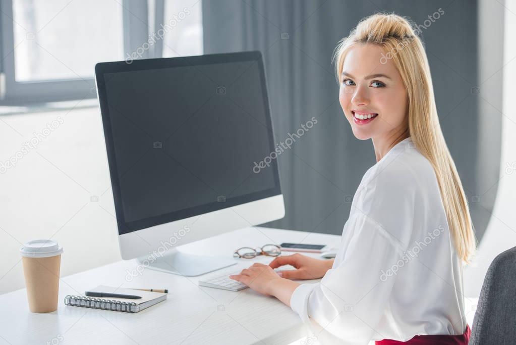 beautiful young businesswoman smiling at camera while working with desktop computer in office
