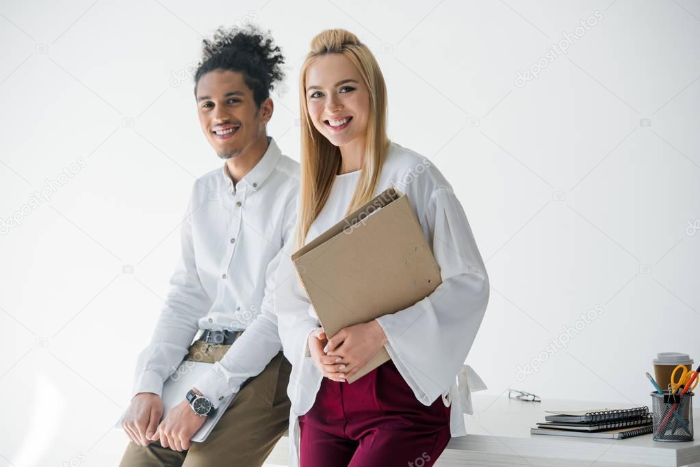 young multiethnic business people with folder and laptop smiling at camera in office