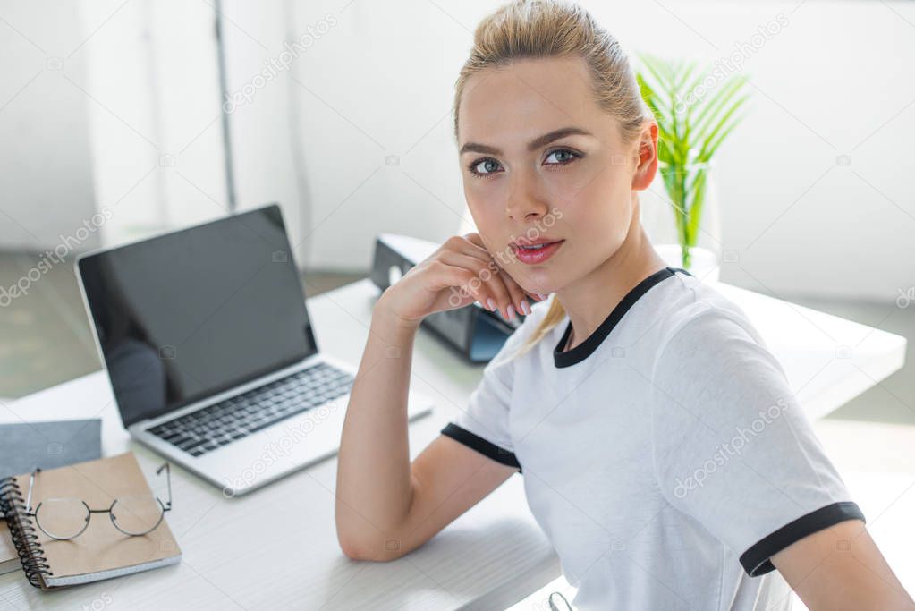 beautiful young woman looking at camera while working with laptop in office