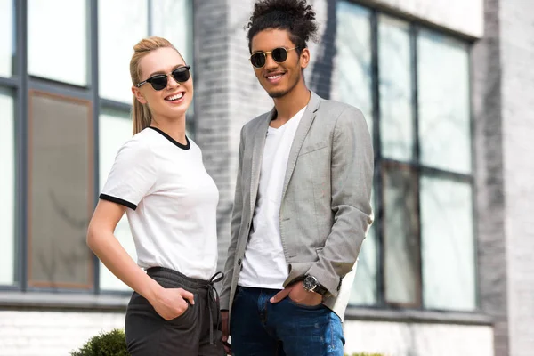 Portrait Beautiful Stylish Multiethnic Couple Sunglasses Standing Hands Pockets Smiling — Free Stock Photo