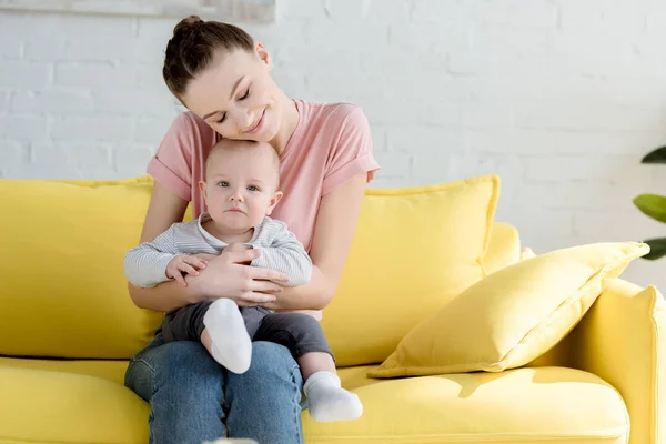 Joven Madre Abrazando Pequeño Hijo Mientras Está Sentado Sofá — Foto de Stock