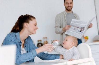 mutlu anne oğul mutfak, gazetenin ardına babasıyla bebek şişe süt ile besleme