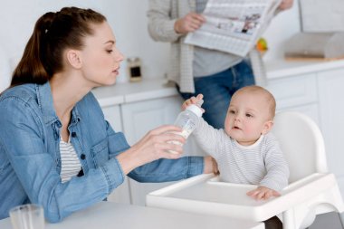 Anne küçük oğlu mutfak, gazetenin ardına babasıyla bebek şişe süt ile besleme