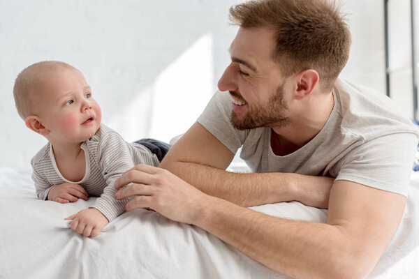 smiling father with little baby boy lying on bed