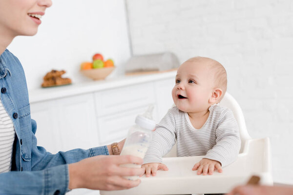 mother feeding little baby boy with milk on kitchen