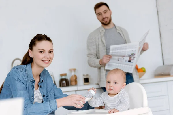 Madre Alimentación Hijo Con Leche Biberón Cocina Padre Con Periódico — Foto de Stock