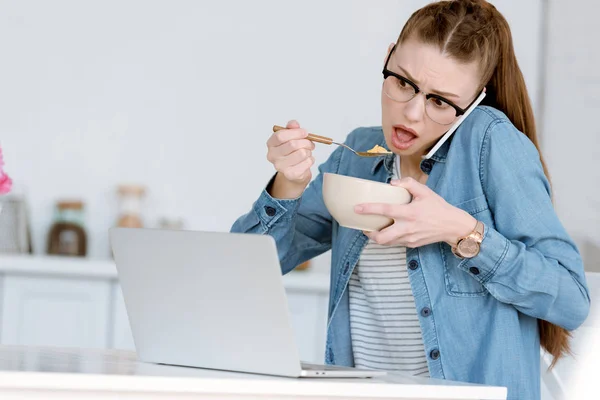 Conmocionó Teletrabajo Mujer Desayunando Mientras Hablaba Teléfono Inteligente Mirando Ordenador — Foto de Stock