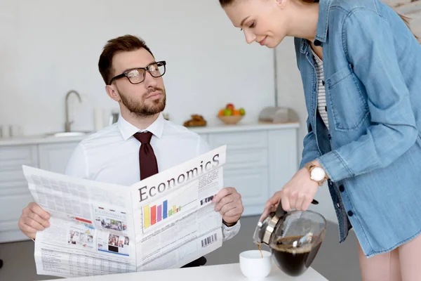 businessman with economics newspaper looking at wife pouring coffee in cup for breakfast