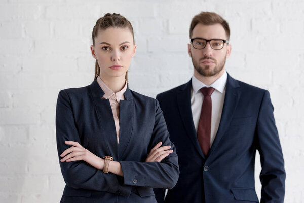 businessman and businesswoman with crossed arms posing near white wall