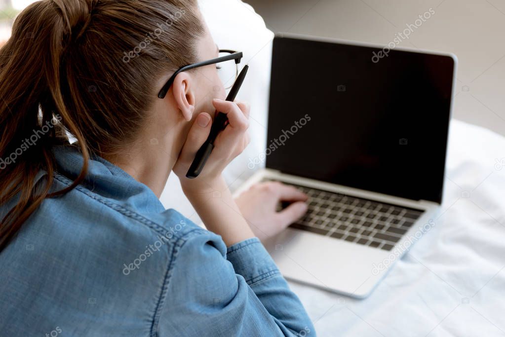back view of young female teleworker using laptop in bedroom