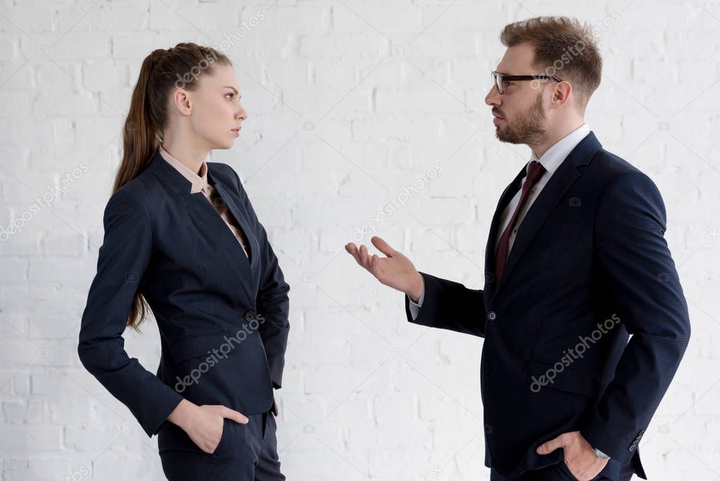 serious businessman and businesswoman in suits discussing near white wall
