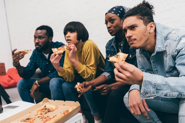 group of young multiethnic friends eating pizza and watching match