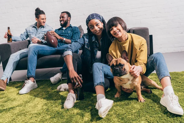 犬とビールとアメリカン フットボールのボールでソファに つの若い男性と敷物の上に座って 人の若い女性の友人  — 無料ストックフォト