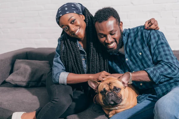 微笑年轻的非洲裔美国人夫妇坐在沙发上与法国斗牛犬 — 图库照片