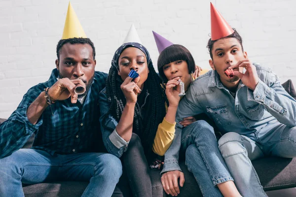 group of multiethnic friends in party hats celebrating with party horns