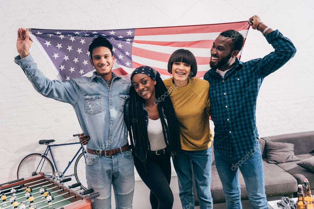 young multiethnic friends with flag of USA standing near table football board 