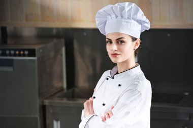 Professional female chef standing with arms folded on modern kitchen clipart
